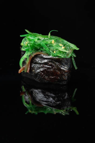 istock Sushi roll with reflection on a black background with green chuka seaweed. A restaurant with Japanese cuisine. 1335030856