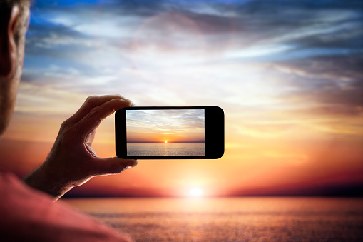 Smartphone camera photographing a sunset across the sea on vacation