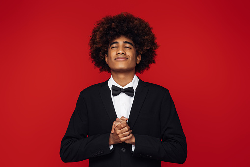 African american man with afro hair wearing the tuxedo and standing over isolated red background