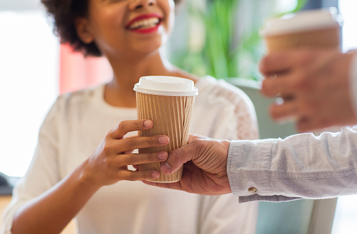 people, drinks and care concept - close up of happy african american woman hand taking coffee cup from man