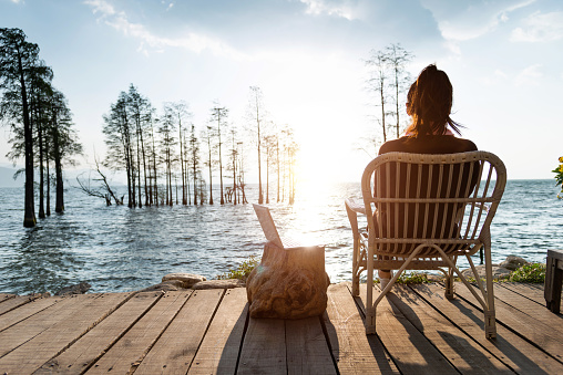 Woman sitting by the lake with a laptop.