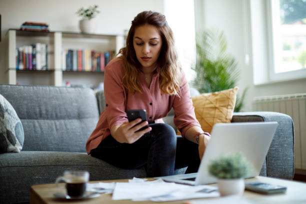 istock Young woman using mobile phone and laptop at home 1335043930