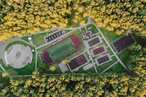 Aerial view of the sports field in the park: football field and training grounds surrounded by trees. High quality drone photo.