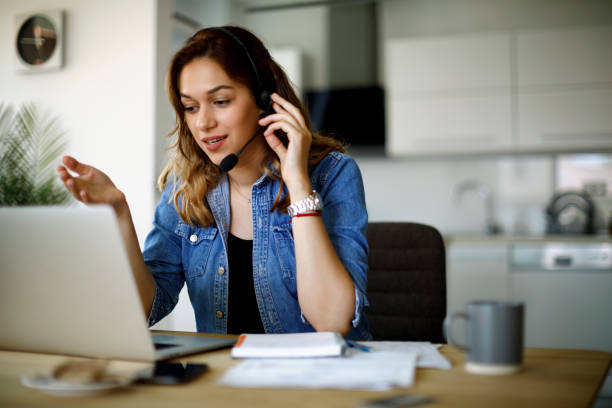 Young woman using a headset and laptop at home office stock photo