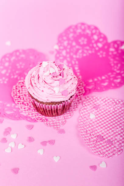 istock Pink cupcakes with heart shaped decorations in a pink background 1335044572