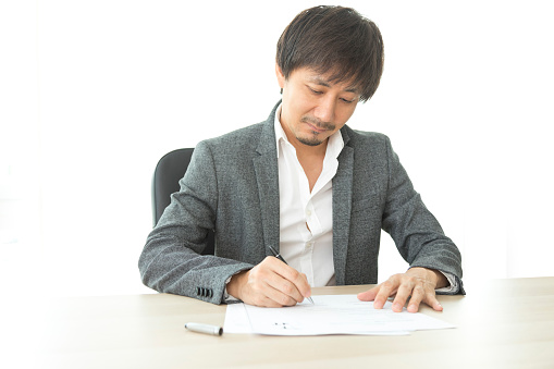 Middle age Asian businessman writing document report in the office. Signing contract.