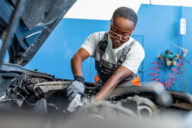 Black woman mechanic working under the hood at repair garage. Portrait of a mechanic at work in his garage or car repair service or auto store, business, maintenance and people concept mechanic working under car stock pictures, royalty-free photos & images
