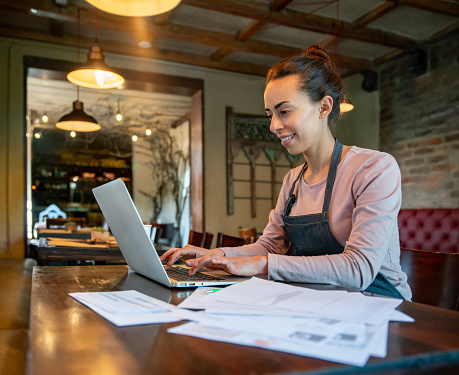 Happy owner working at a restaurant doing the bookkeeping using her laptop  - small business concepts