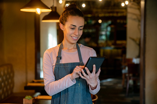 Happy Latin American waitress working at a restaurant using a tablet to write down the orders - food service concepts