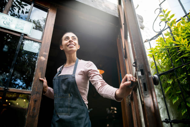 Waitress working at a restaurant and opening the door Happy Latin American waitress working at a restaurant and opening the door to receive customers - food and drink concepts reopening photos stock pictures, royalty-free photos & images