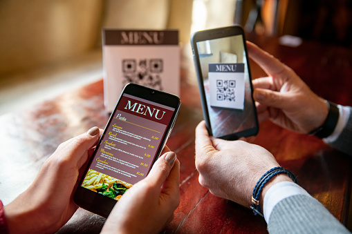 Close-up on a couple at a restaurant scanning the menu with QR codes using their cell phones - new normal concepts. **DESIGN OF QR CODE AND MENU WERE MADE FROM SCRATCH BY US**