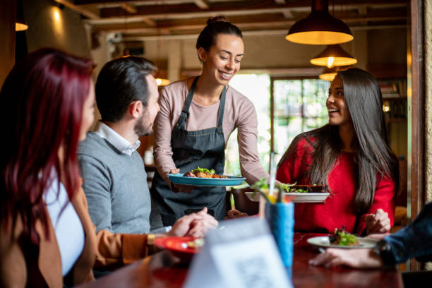 camarera que sirve comida a un grupo de clientes en un restaurante - restaurant fotografías e imágenes de stock