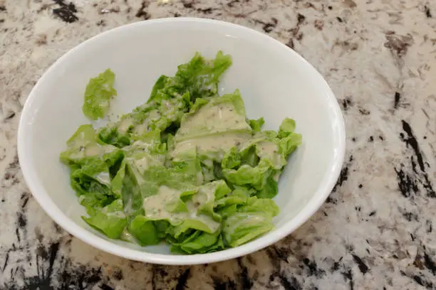 Ranch salad dressing on lettuce leaves that were just harvested from an indoor garden. Closeup of fresh green lettuce leaves with creamy ranch dressing in a white bowl on a granite counter.