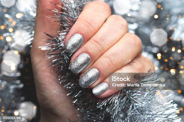 Hand With Silver Glittered Nails On Christmas Tinsel Background With Blurred Lights Bokeh Stock Photo - Download Image Now