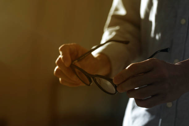 Close up of man hand holding eyeglass in dark background.