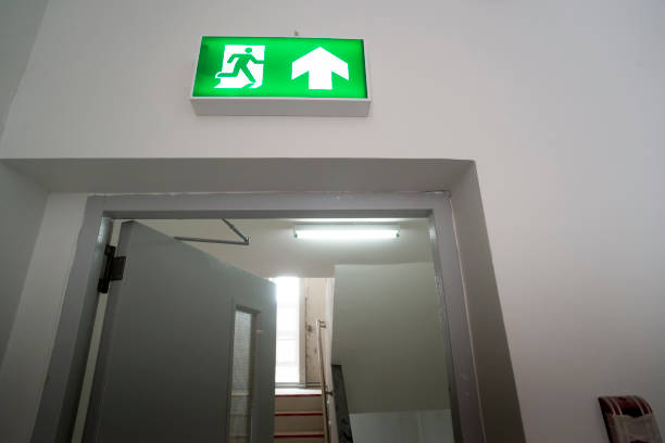istock Sign : Emergency exit sign at path way indoor building public facility that emergency escape route is left. (fire, building, health or safety) require exit signs to be permanently lit 1335059839