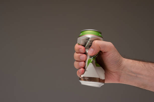 Caucasian male holding a crushed tin metal beer can. Close up studio shot, isolated on brown background stock photo
