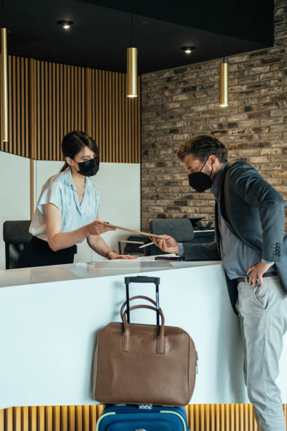 istock Female Hotel Receptionist Giving Check In Registration Forms to Guest During Coronavirus Pandemic 1335061119