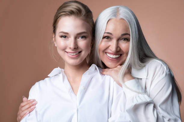 smiling mature mother and young adult girl daughter hugging, two female generations bonding. mother's day concept - mature women model bildbanksfoton och bilder