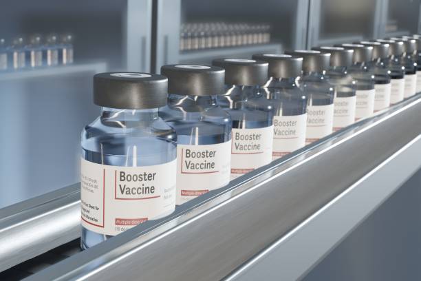 Vials of booster vaccine on conveyor in pharmaceutical factory Multiple vials in a row on a conveyor belt in a pharmaceutical factory.  There are additional supplies in storage cabinets in the background. booster dose photos stock pictures, royalty-free photos & images