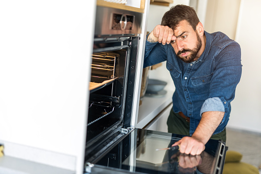 Worried repairman examining and fixing an oven in the kitchen.