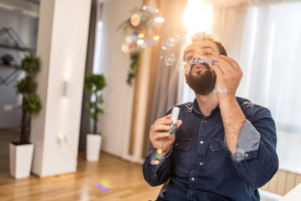 Happy young man blowing bubbles at home.