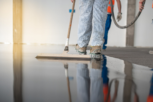 Worker working on the floor of an industrial building. Construction worker producing grout and finishing wet concrete floor.