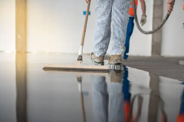 Photo of Worker working on the floor of an industrial building. Construction worker producing grout and finishing wet concrete floor.