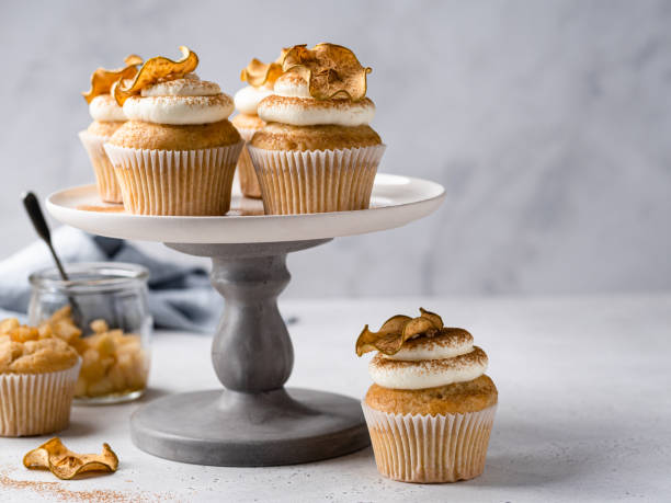 Apple cupcakes decorated with cream cheese frosting and dried apple slices. Close up view.  Copy space. Grey concrete background. Delicious and festive autumn, fall or summer cooking. Cinnamon spicy apple cakes with whipped cream and cinnamon powder. apple cinnamon pancake stock pictures, royalty-free photos & images