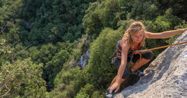 vista de jovem subindo rosto de rocha ensolarada - climbing rock climbing women determination - fotografias e filmes do acervo