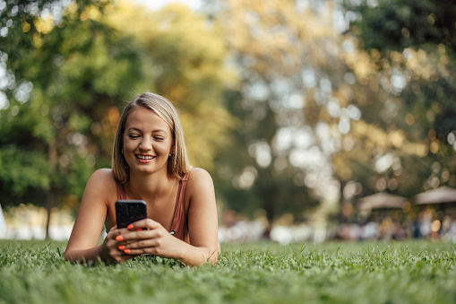 Smiling woman lying on a grass and using smart phone, portrait. Enjoying summer.