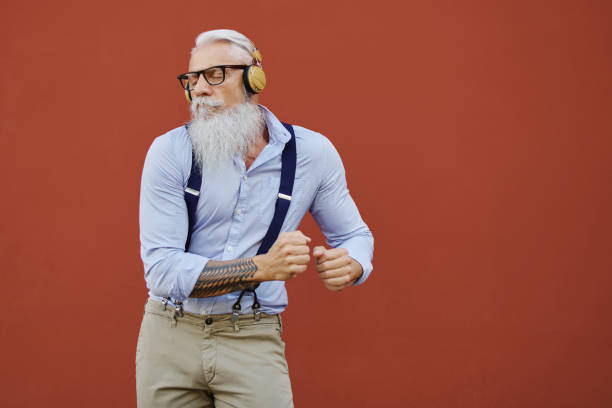 hipster caucasico felice vecchio balla ascoltando musica in città - senior adult energy people confidence foto e immagini stock