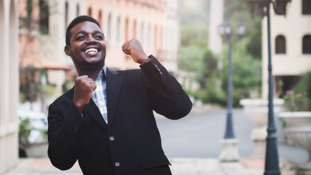 istock Excited african businessman keeping arms raised and expressing positivity while standing outdoors with the building in  background.Celebrating success concept 1335080501