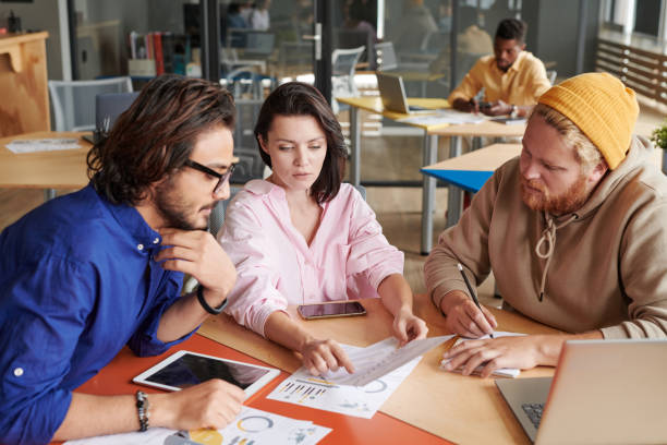 istock Attractive young woman pointing at paper data while analyzing chart with colleagues in shared workplace 1335084894