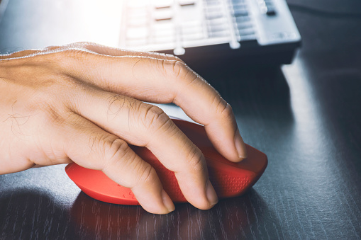 Human hand using computer mouse with a red color on desk