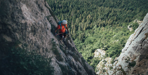 Climber on via ferrata trail Climber on via ferrata trail, crossing a steep mountain edge. rock climbing stock pictures, royalty-free photos & images