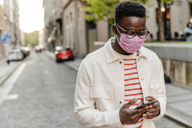 istock African-American young man wearing protective face mask, walking and using mobile phone 1335098957