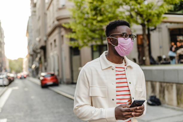istock African-American young man wearing protective face mask, walking and using mobile phone 1335098958