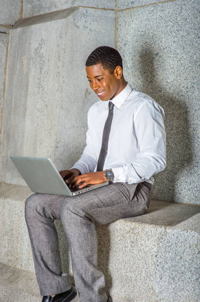 istock Young black businessman sitting outside office building, working on laptop computer 1335099043