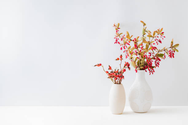istock Home interior with decor elements. Colorful autumn leaves and red berries in a vase on a light background 1335099280