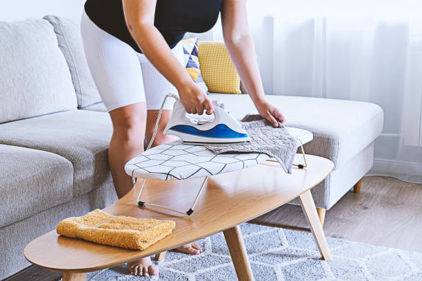 istock Woman ironing on small ironing board on table in light living room 1335110419