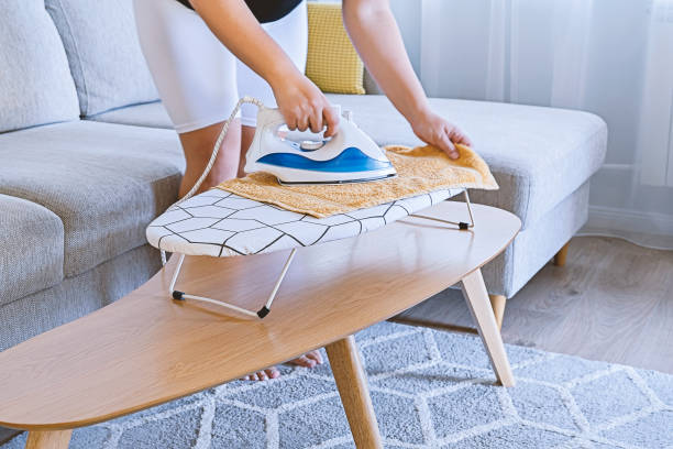 istock Woman ironing on small ironing board on table in light living room 1335110420