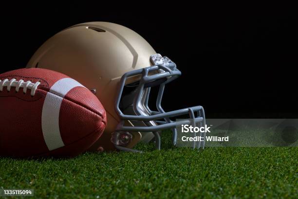 Low Angle View Of Football And Gold Helmet On Grass Field With Dark Background Stock Photo - Download Image Now