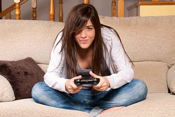 Young female playing video-games concentrating on sofa at home stock photo