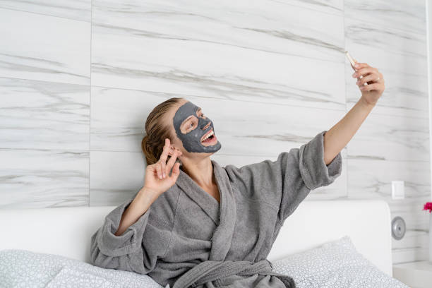 istock Woman with face mask relaxing sitting on the bed using mobile device 1335117496
