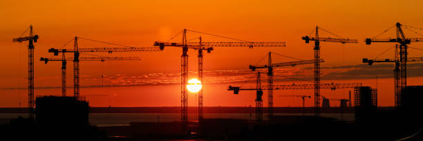 Wide panoramic industrial landscape of a many  of construction tower cranes against a flame bright red and orange sunset. stock photo