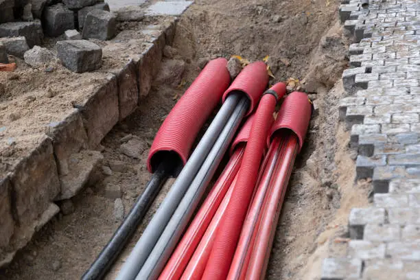 A large number of electric and high-speed Internet Network cables in red corrugated pipe are buried underground on the street covered with cobblestones. Construction site with A lot of  Gigabit communication Cables Network Buildout