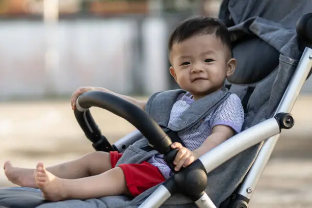 Photo of Happy and cute Asian Chinese baby boy sitting on stroller at park during evening