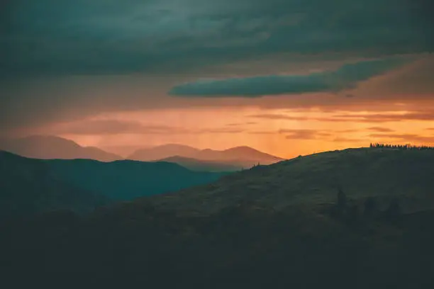 Photo of Atmospheric landscape with silhouettes of mountains with trees on background of orange dawn sky. Colorful nature scenery with sunset or sunrise. Sundown paysage in vintage colors and faded tones.