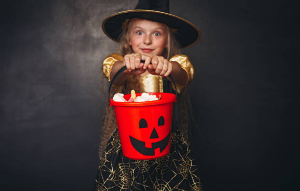 Amazed little witch with red pumpkin bucket